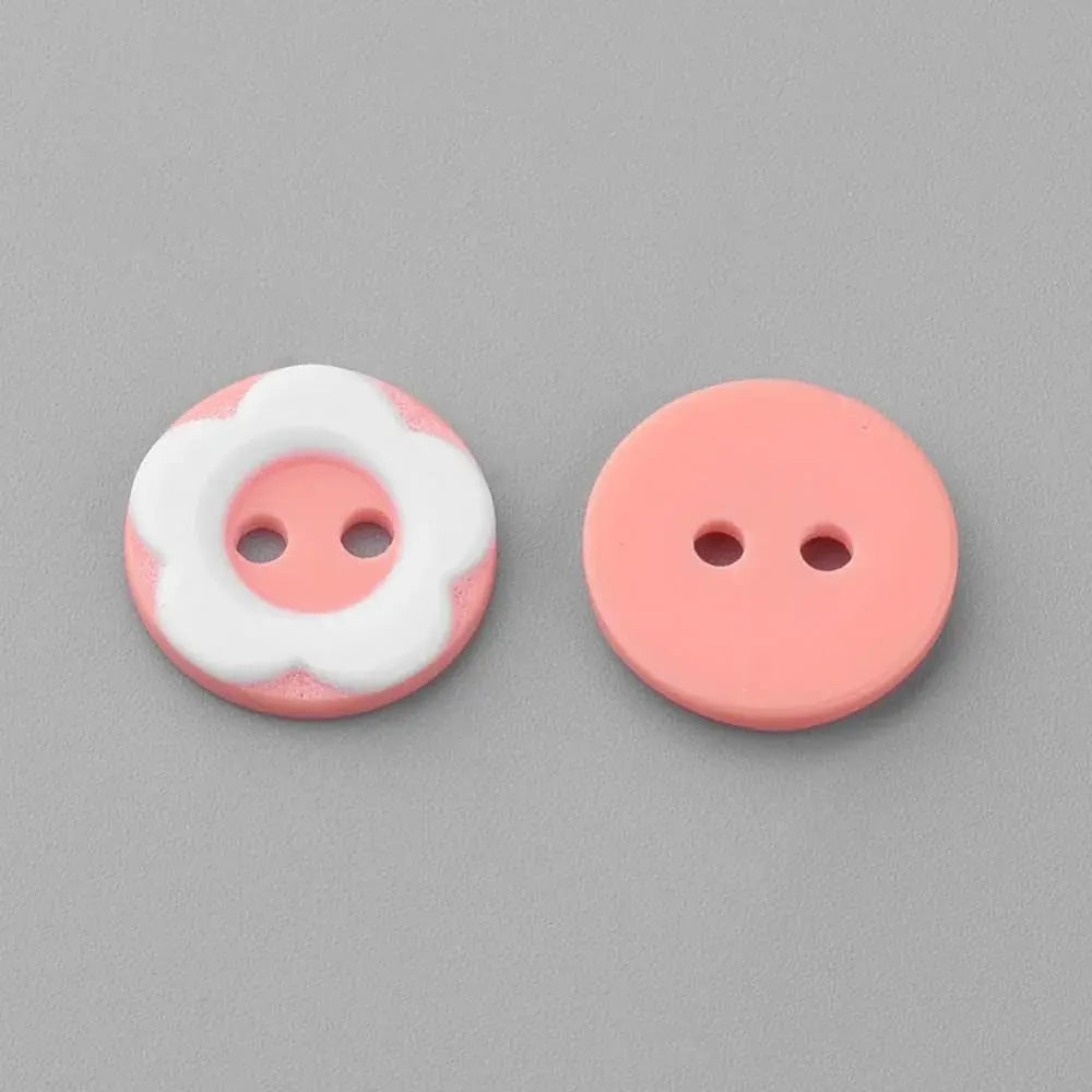 Two pink, two-hole buttons, one with a white flower design.