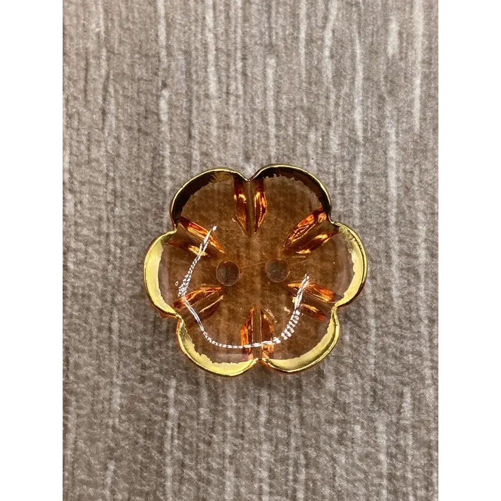 Flower-shaped, amber-colored button with gold trim.