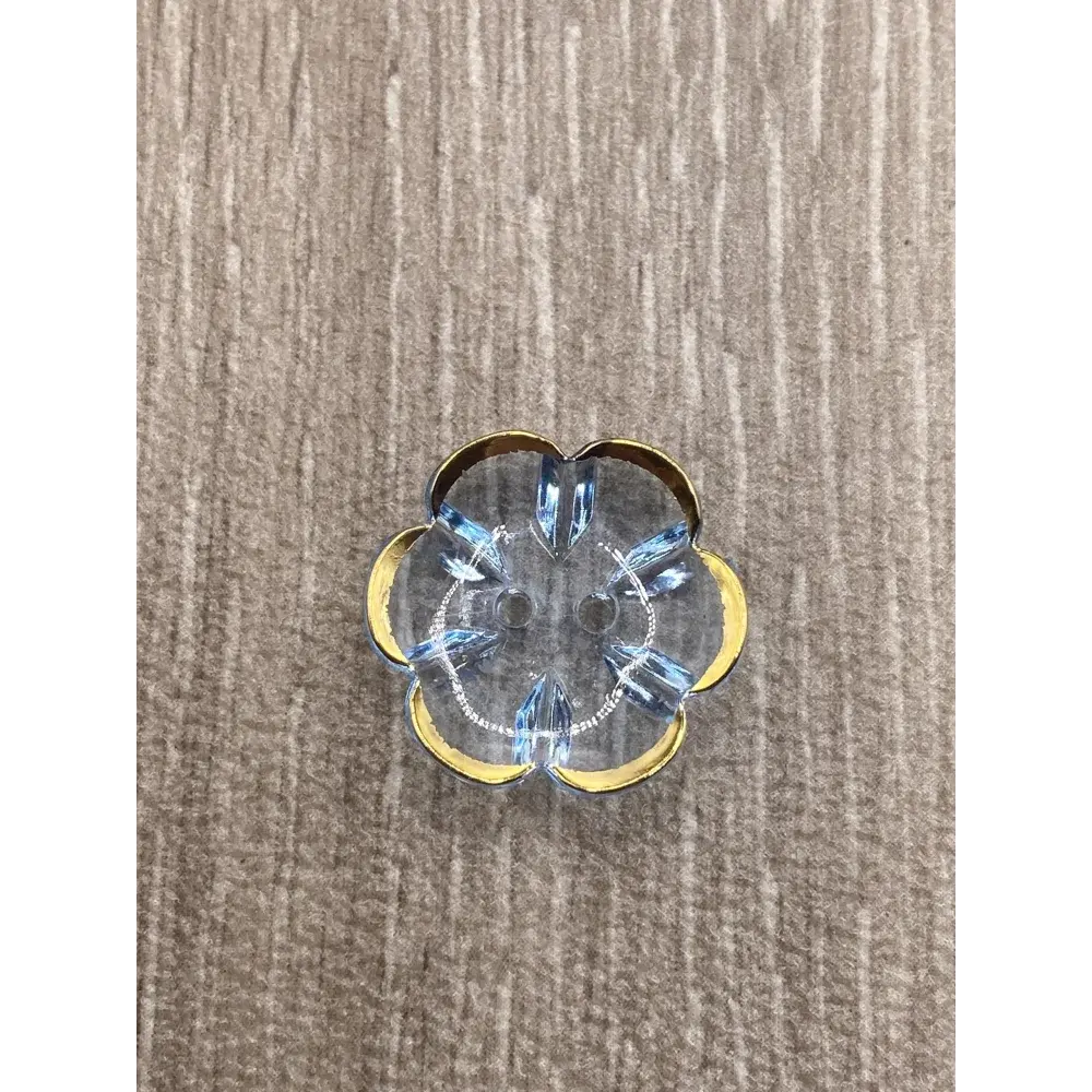 Flower-shaped, clear button with gold trim and blue crystal accents.