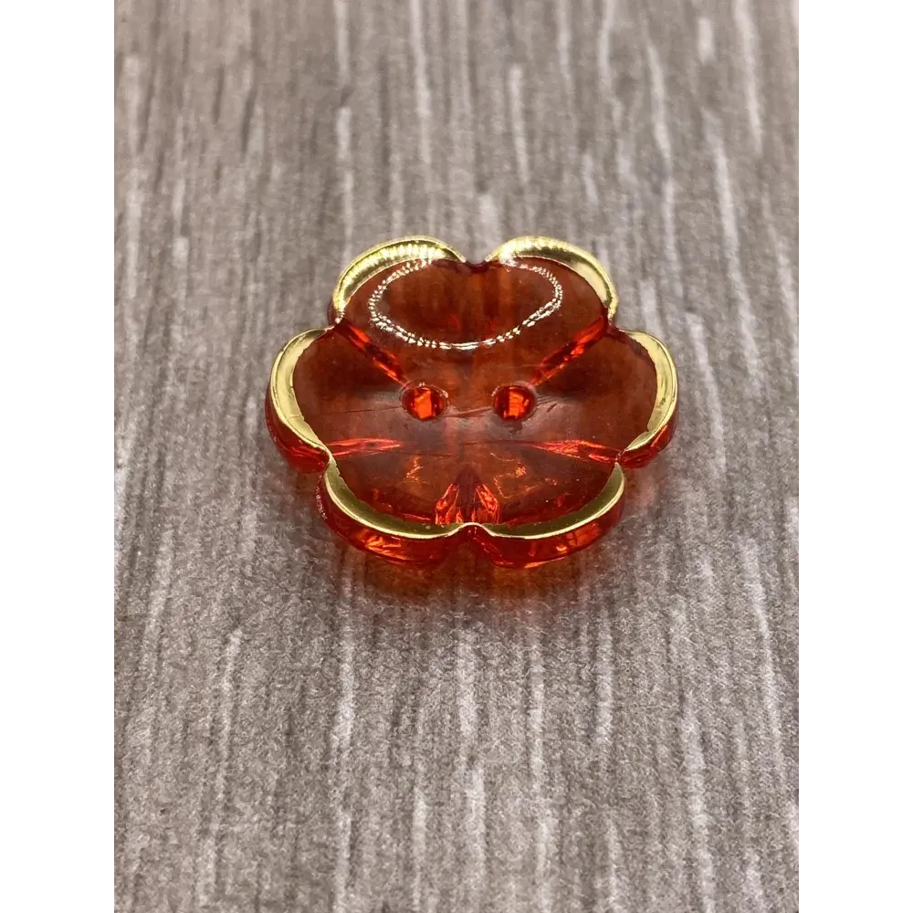 Translucent red flower-shaped button with gold trim.