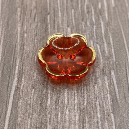 Translucent red flower-shaped button with gold trim.