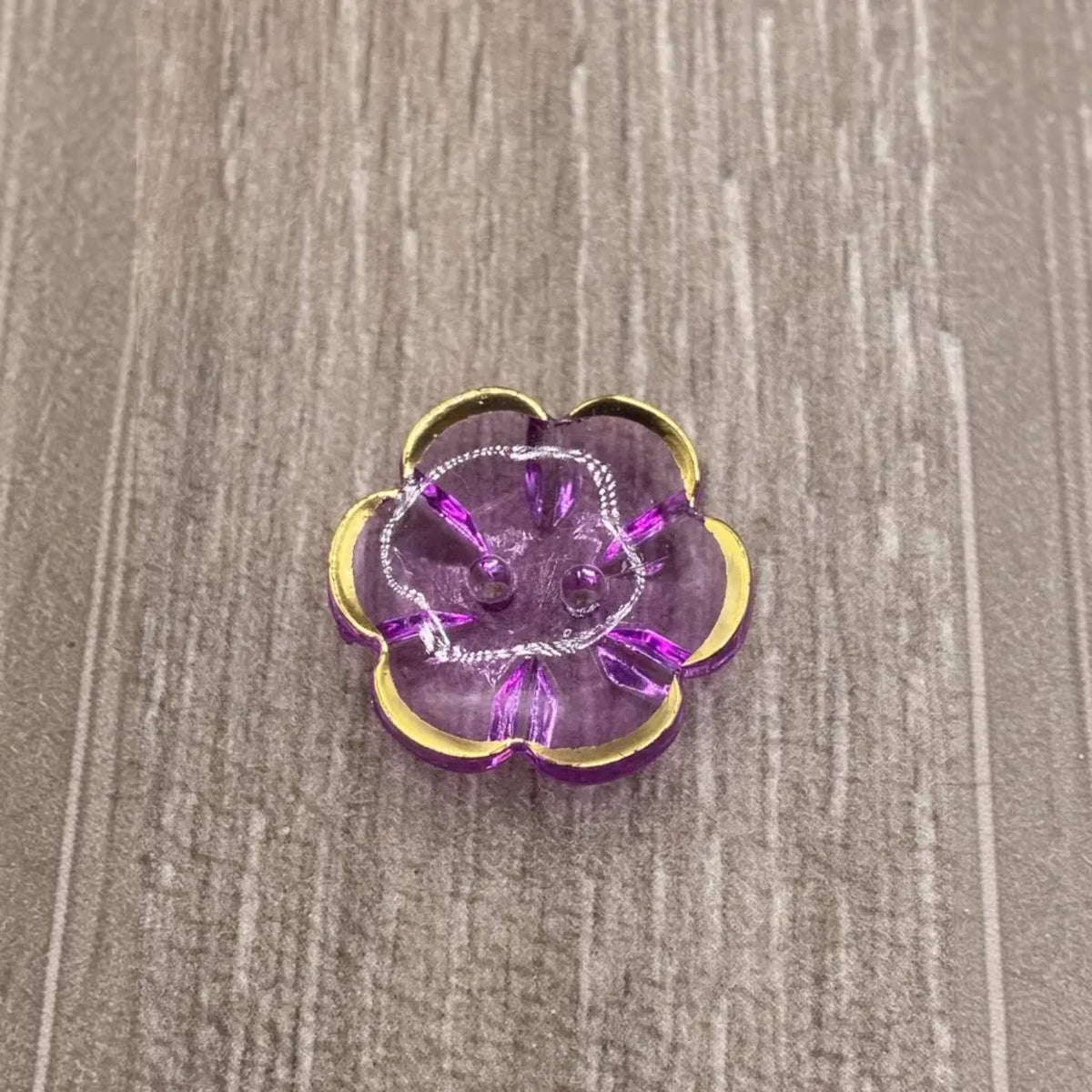 Purple flower-shaped button with gold trim.