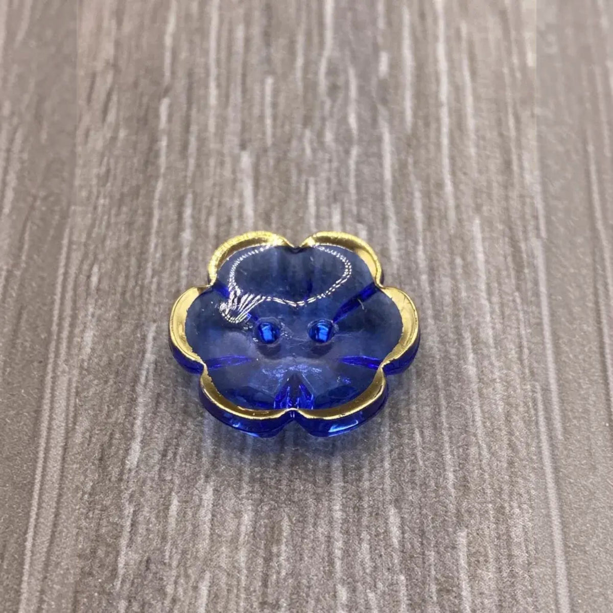 Blue flower-shaped button with gold trim.