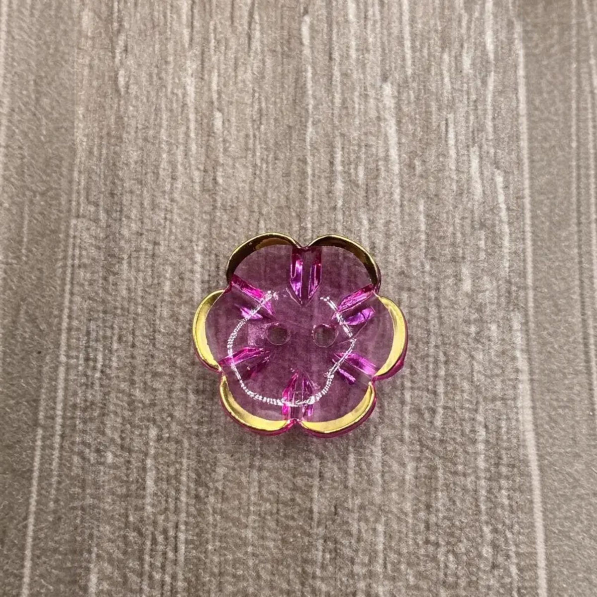 Translucent pink flower-shaped button with gold trim.