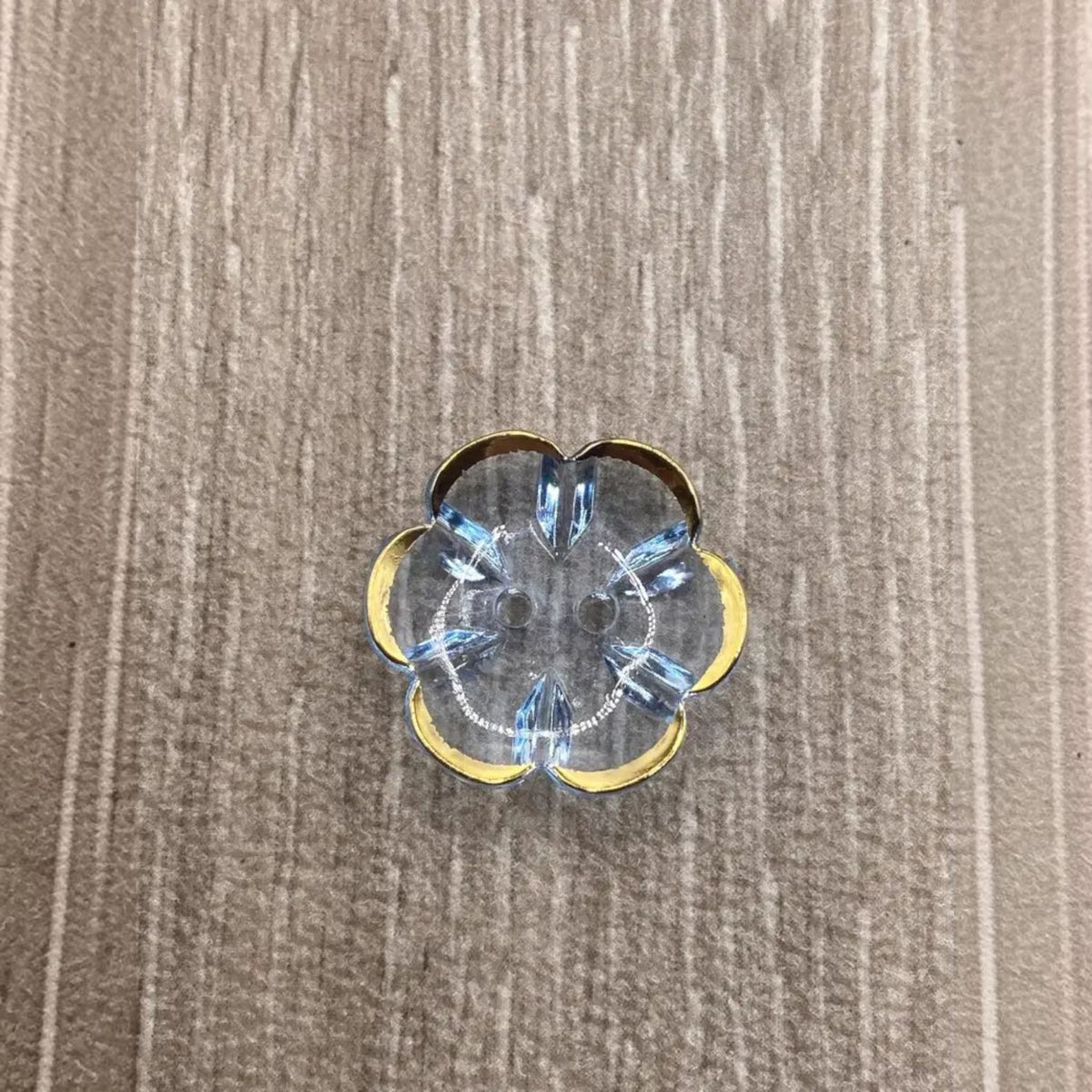 Flower-shaped, clear button with gold trim and blue crystal accents.