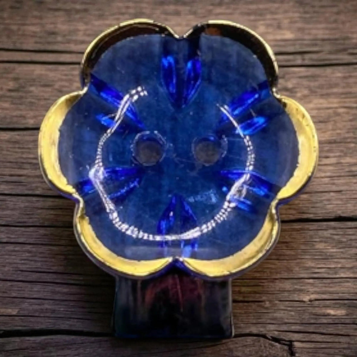 KnitForLess 13mm baby blue flower-shaped acrylic button with a gold rim and two-hole design on a wooden surface.
