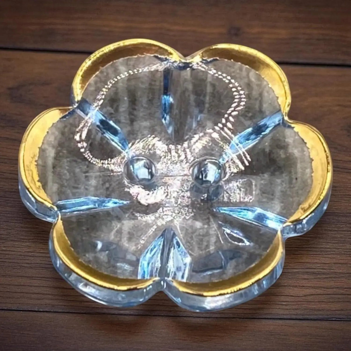 KnitForLess 13mm baby blue flower-shaped acrylic button with a gold rim and two-hole design on a wooden surface