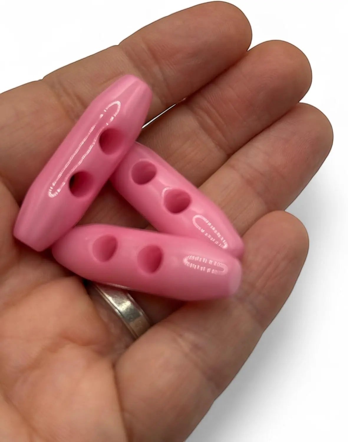 KnitForLess baby pink 38mm plastic toggle buttons with 2-hole design held in a hand