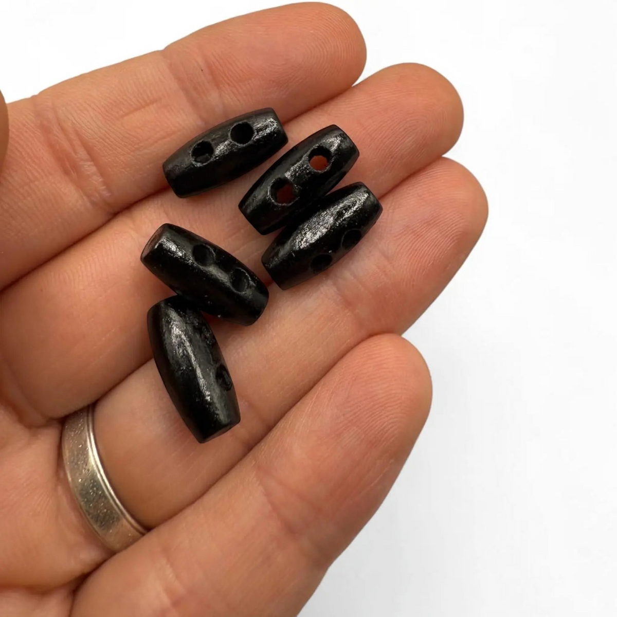 KnitForLess black wooden mini barrel toggle buttons held in a hand for scale, perfect for baby cardigans and crafts.