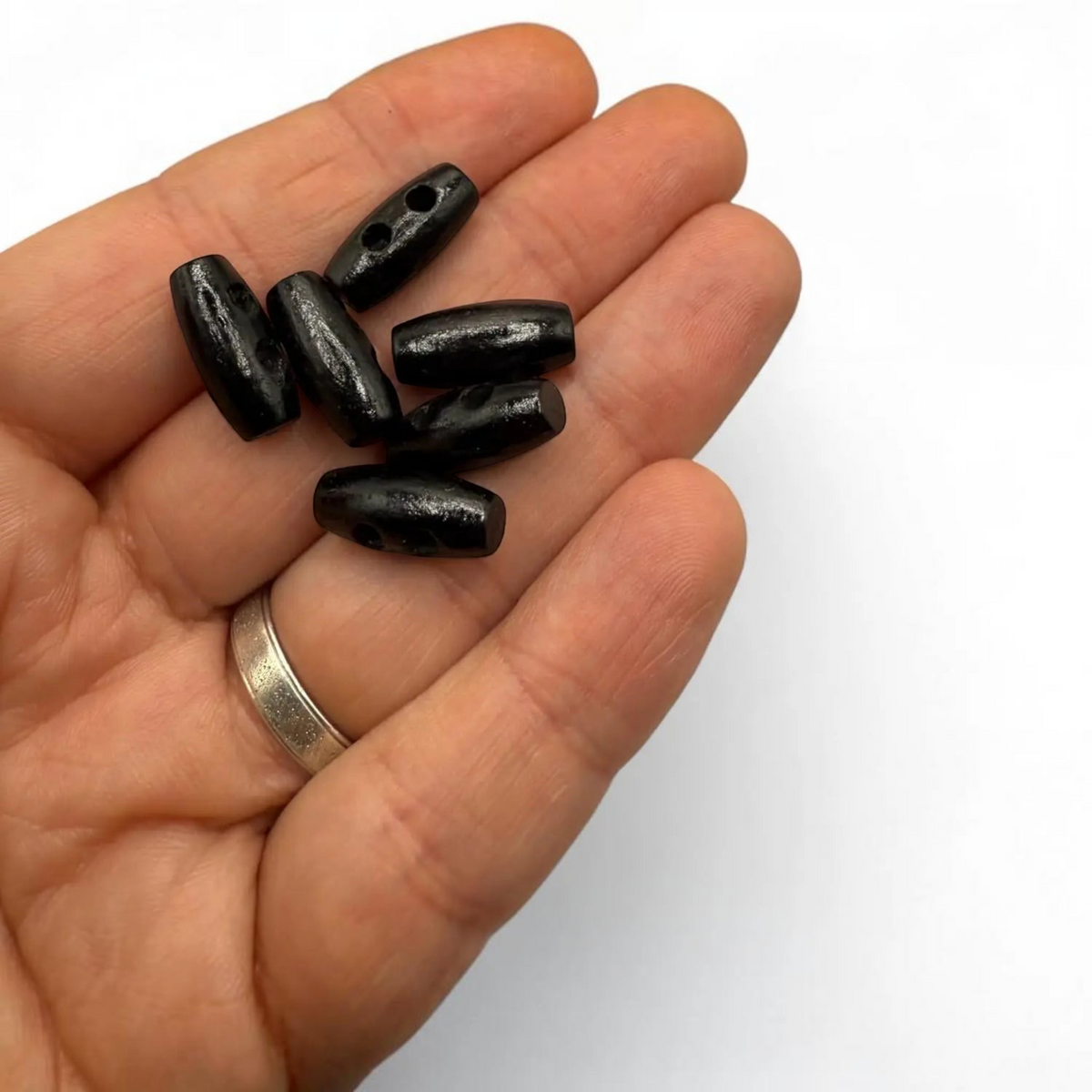 KnitForLess black wooden mini barrel toggle buttons held in a hand for scale, perfect for baby cardigans and crafts.