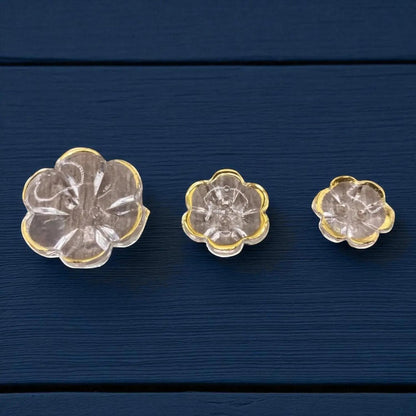 KnitForLess clear acrylic flower-shaped buttons with gold rims in various sizes on a dark blue wooden surface