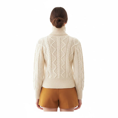 Back view of a woman wearing a KnitForLess cream aran cable knit jumper with a turtleneck and mustard shorts.