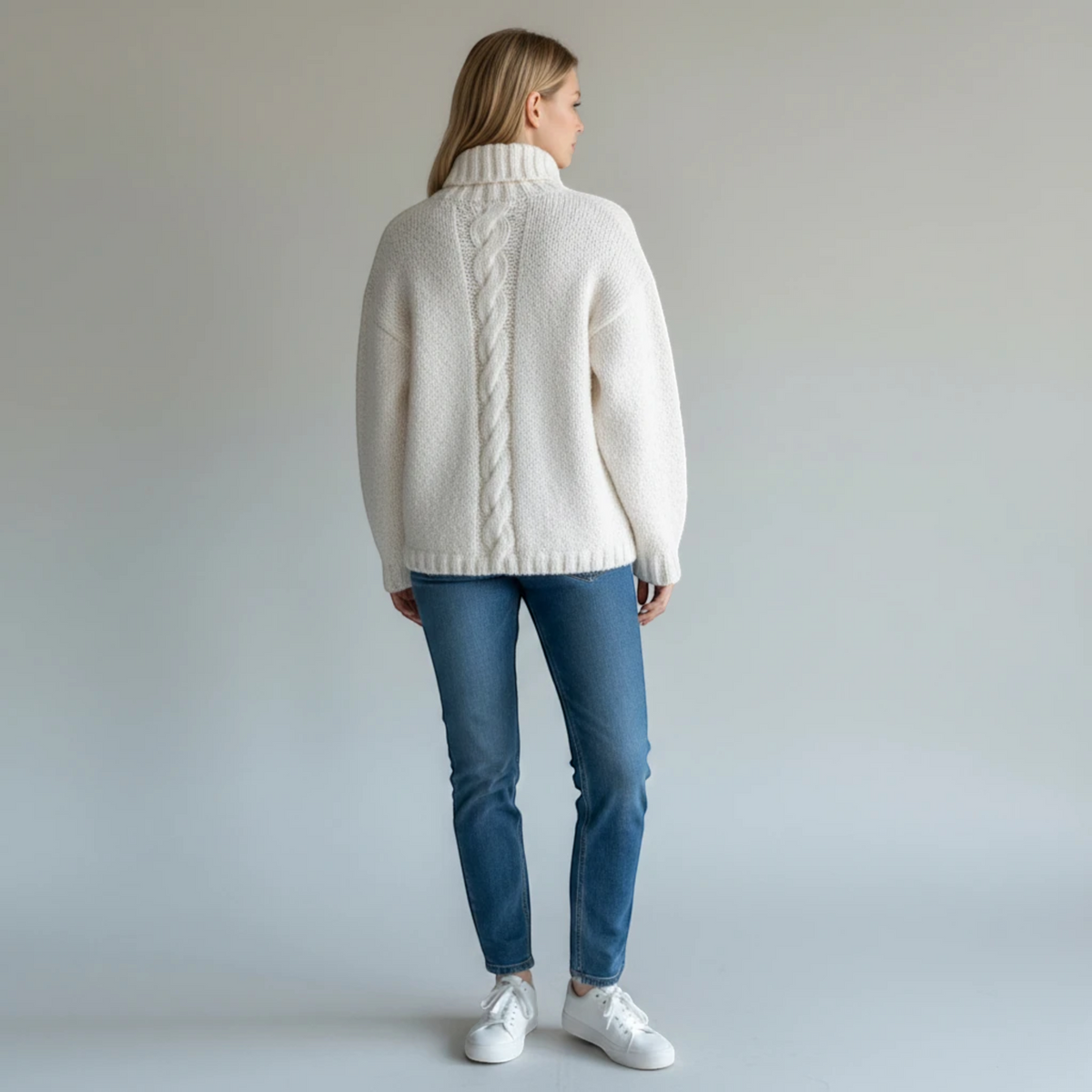Woman wearing a KnitForLess cream cable-knit sweater with a turtleneck, viewed from the back against a grey background.