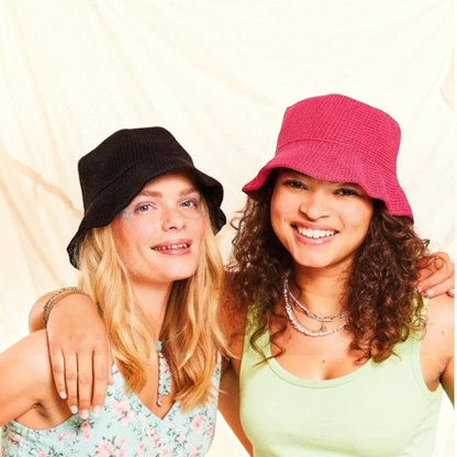 Two women wearing handmade KnitForLess crochet bucket hats in black and bright pink for a stylish summer look.