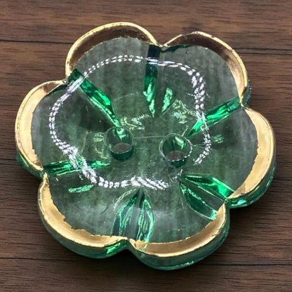 KnitForLess 13mm green flower-shaped acrylic button with a gold rim and two-hole design on a wooden surface