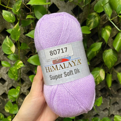 KnitForLess Himalaya Super Soft DK acrylic yarn in baby pink held in hand against a green leafy background.