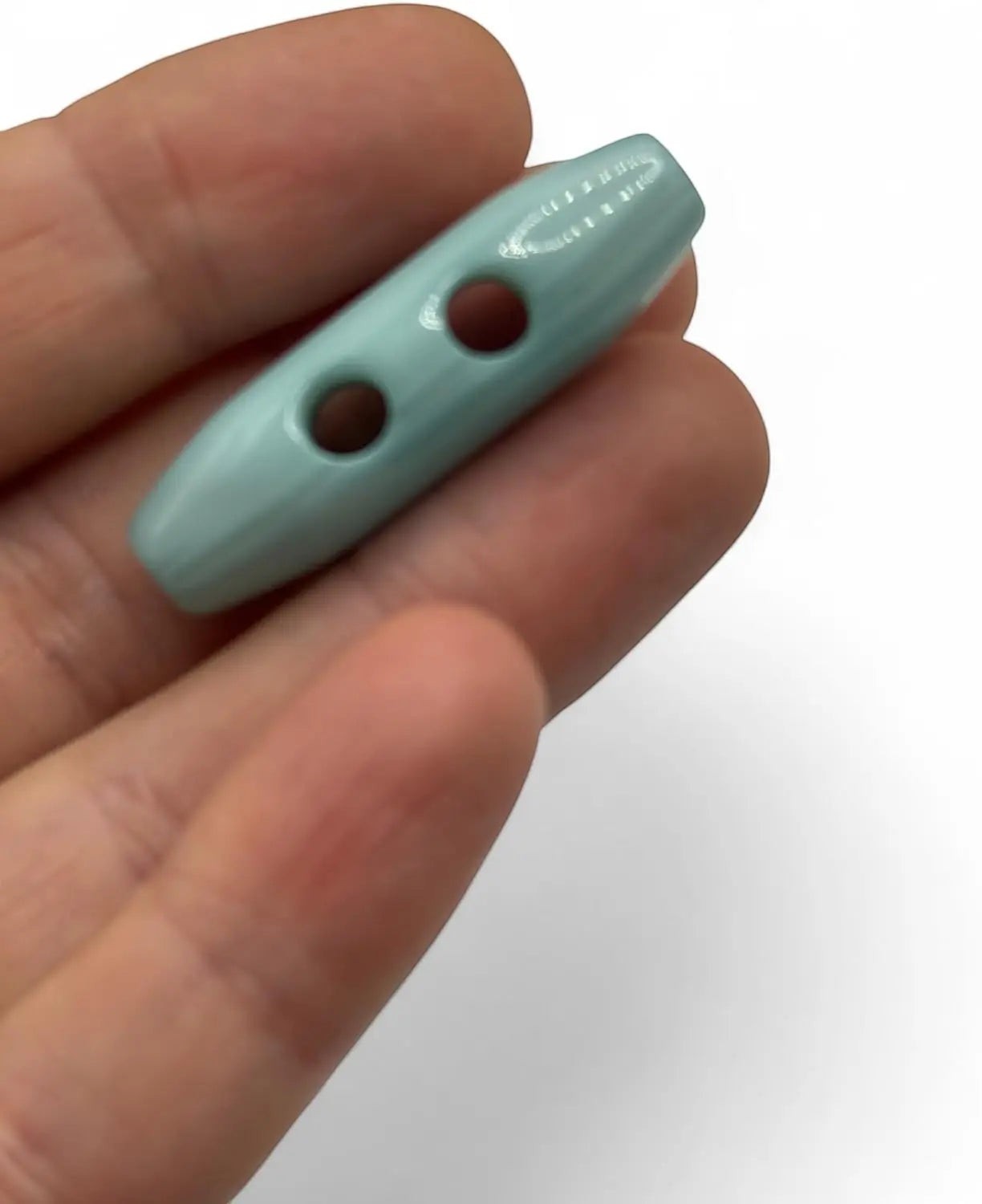 KnitForLess light blue classic toggle button with a smooth glossy finish held in a hand for knitwear and coats.