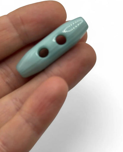 KnitForLess light blue classic toggle button with a smooth glossy finish held in a hand for knitwear and coats.