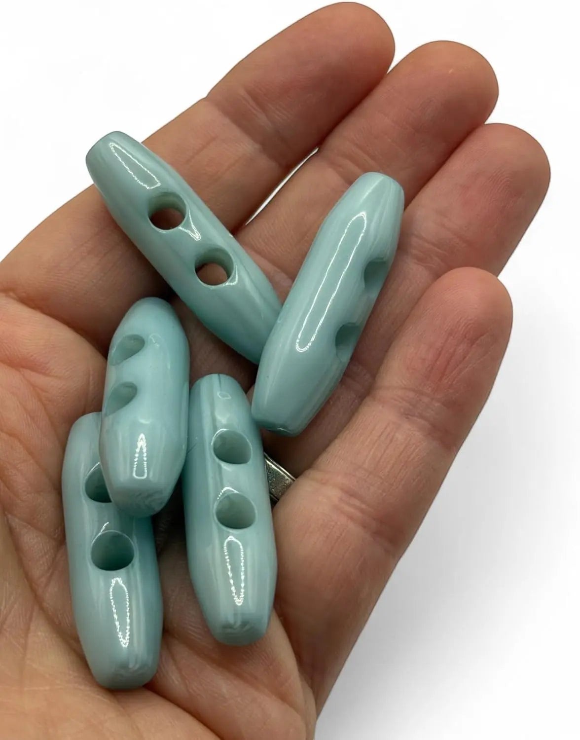 KnitForLess light blue toggle buttons with a smooth glossy finish held in a hand for knitwear and sewing projects