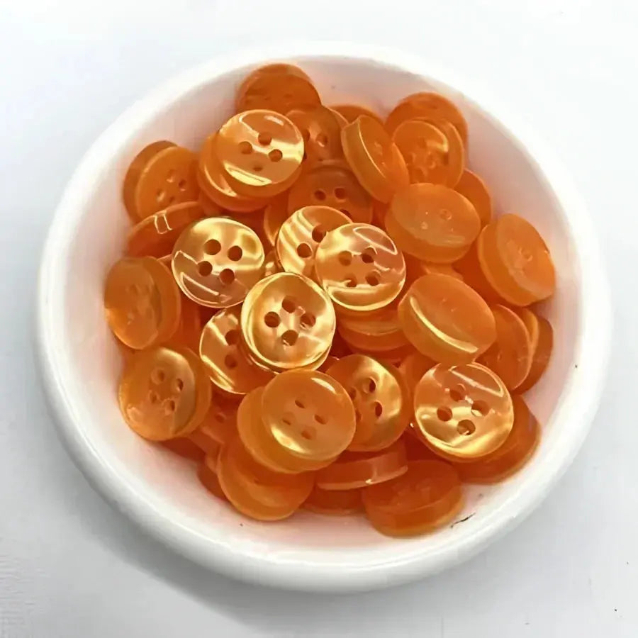 Orange, four-hole, shiny buttons in a bowl.