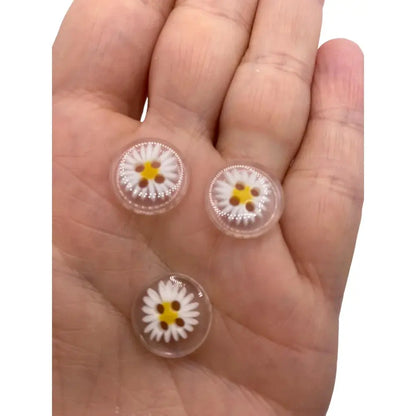 Three daisy-themed glass cabochons.