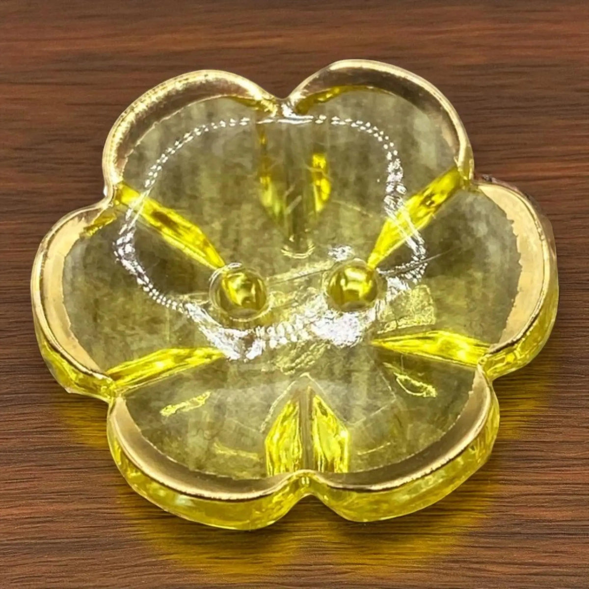 KnitForLess yellow flower-shaped acrylic button with a gold rim and two-hole design on a wooden surface